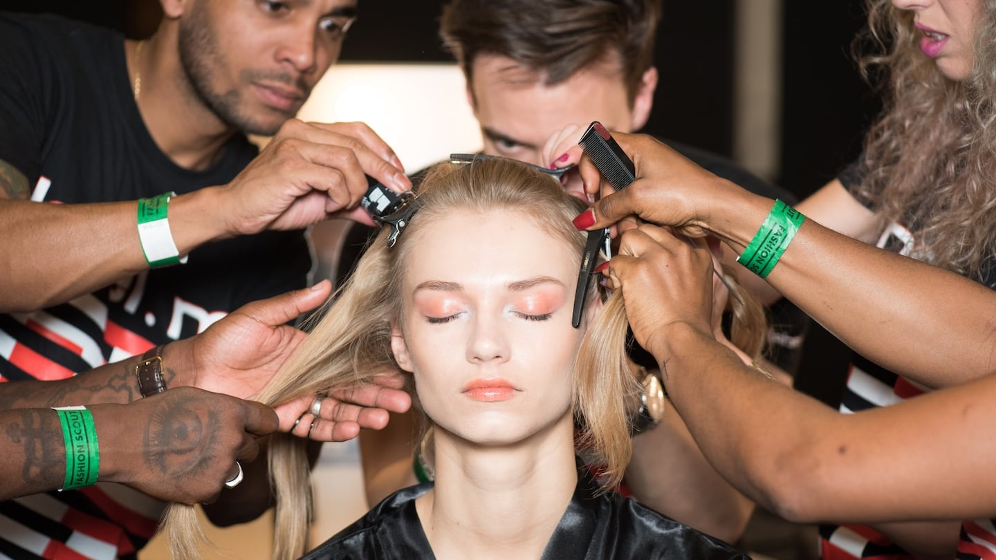 Hairstylists clip and style a models hair backstage at a fashion show.