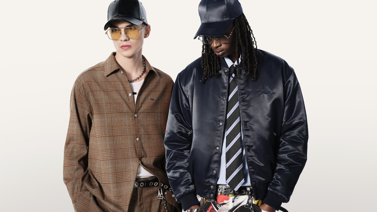 Two models wear clothes by 9dcc, one in a black bomber jacket and the other in a brown plaid oversized shirt.