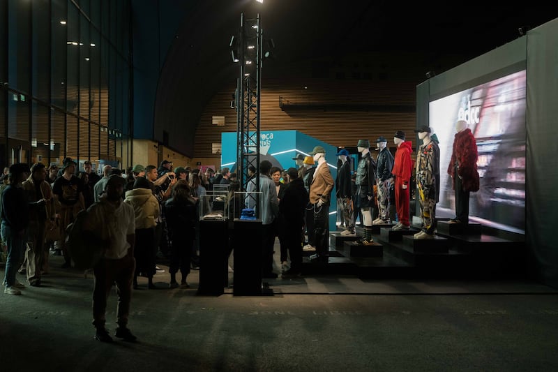 A crowd stands in an industrial space where mannequins at the front are in looks by 9dcc.
