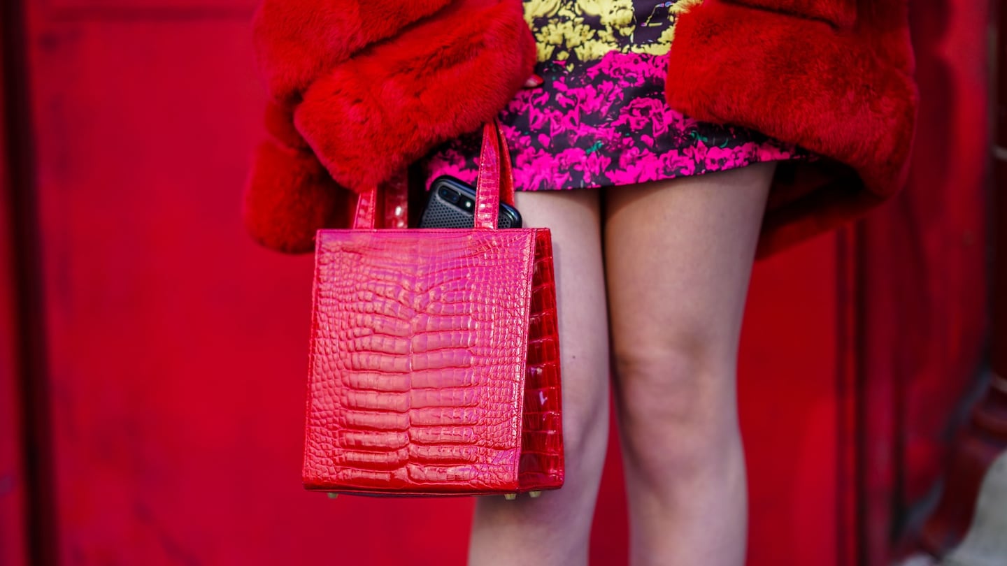 A guest in a red fur coat and pink skirt carries a red crocodile leather bag during London Fashion Week in 2018.
