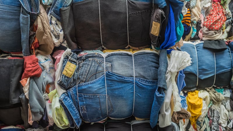 Bales of clothes tied with string are piled up next to each other.